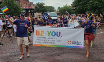 Quantum Workplace employees participating in a Pride parade and holding a sign that says "Be You".