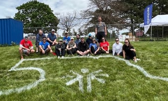Fifteen Quantum Workplace employees volunteering with the Special Olympics and posing on a grass lawn.