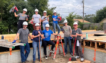 Nine Quantum Workplace employees volunteering at a house construction site with hard hats and power tools.