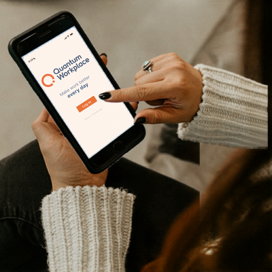 A person holds a smartphone displaying the Quantum Workplace app login screen. The app's tagline reads 