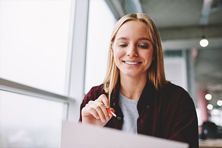 Woman looking at piece of paper while smiling and holding a pen