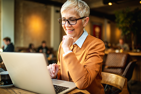 Woman wearing glasses smiling while looking at her computer in a coffee shop