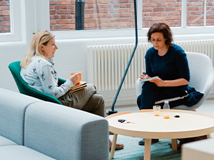 Two women talking and holding notebooks during a 1 on 1 meeting