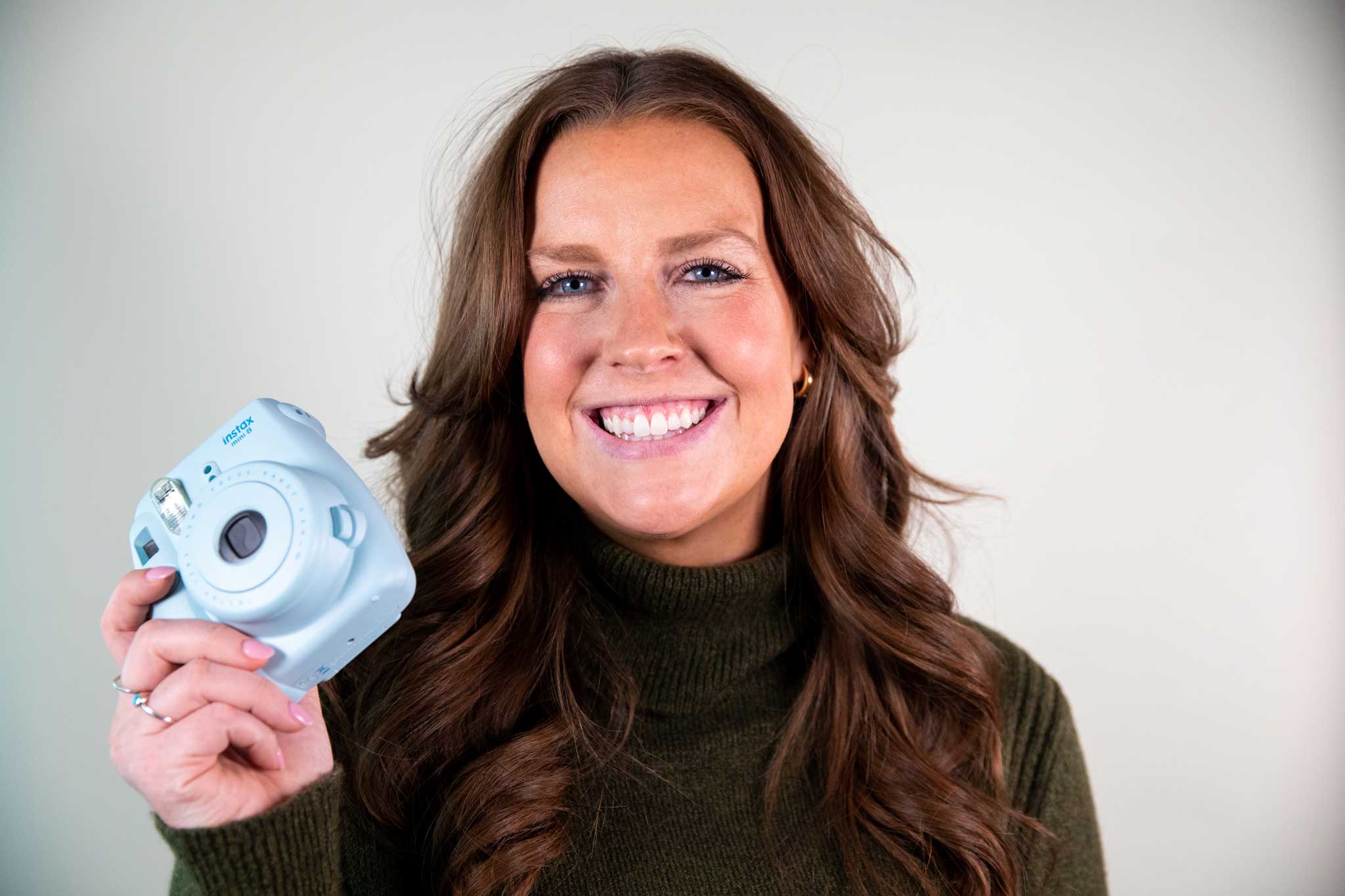 A Quantum Workplace employee smiling and holding a blue polaroid camera.