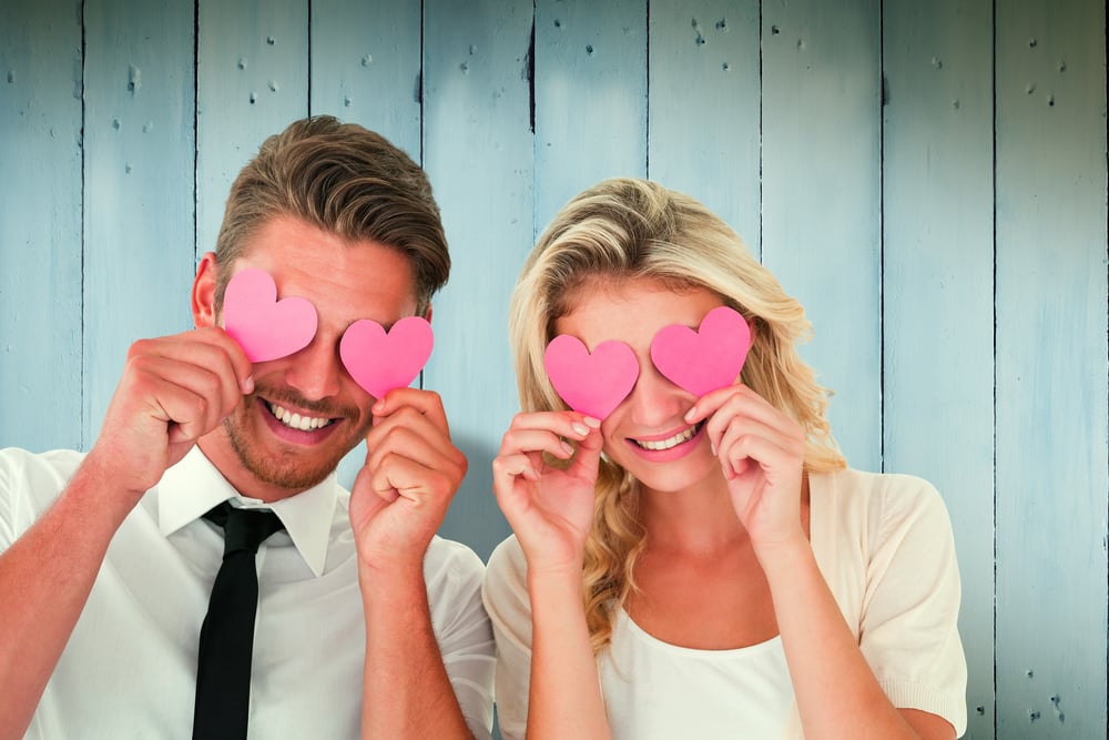Attractive young couple holding pink hearts over eyes against wooden planks-1